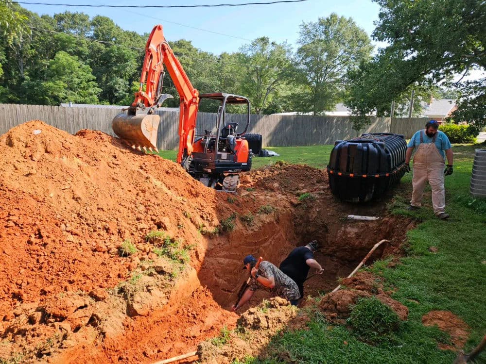 Excavation in backyard with workers digging and machinery for septic system installation.