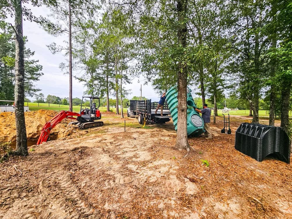 Excavation site with machinery, storage containers, and tree cover in a rural landscape.