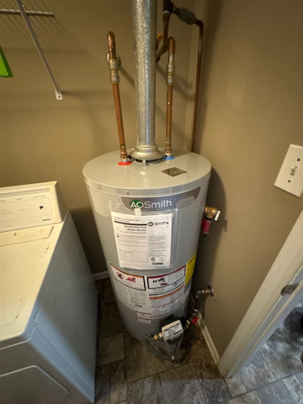 AO Smith water heater installed in a laundry room with pipes and connections.