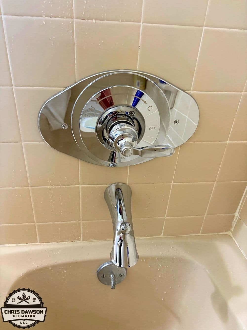 Shiny chrome bathtub faucet and control for hot and cold water in a beige tiled bathroom.