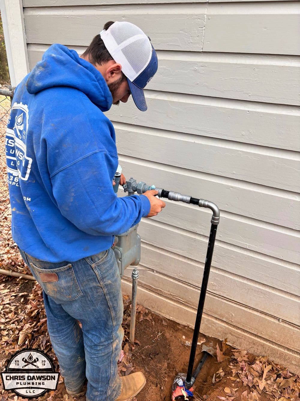 Plumber installing gas meter next to home foundation with tools at Chris Dawson Plumbing.