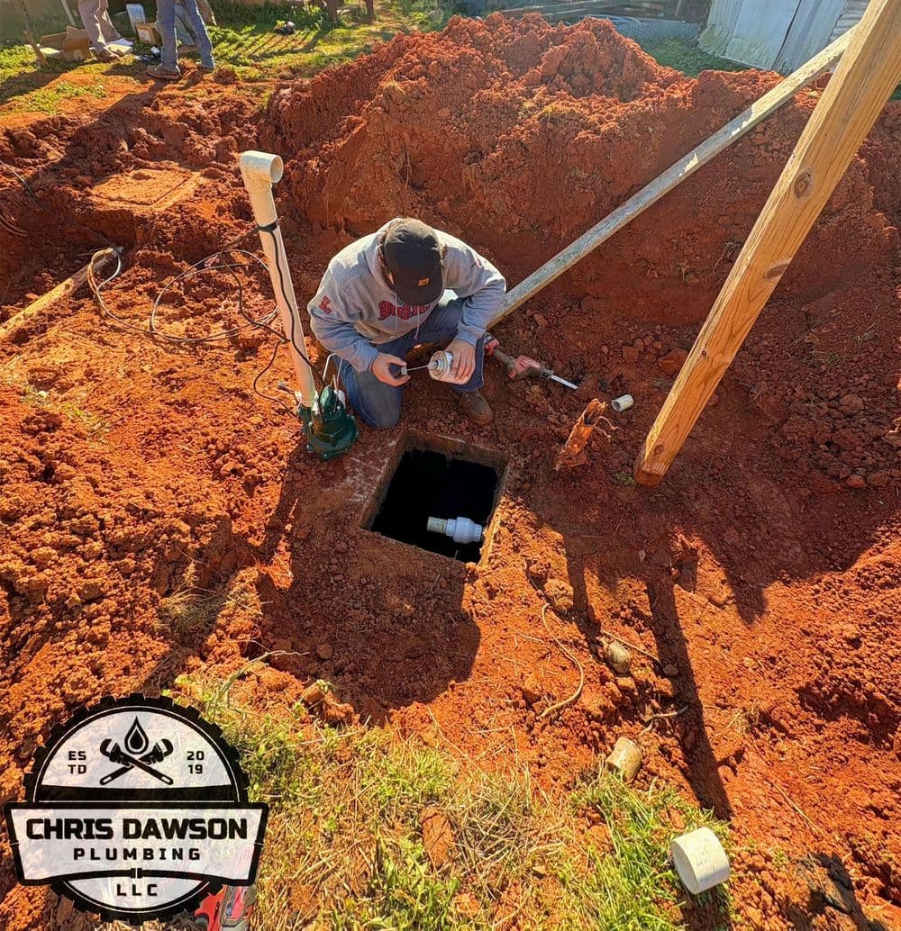 Plumber inspecting a drainage system installation in a freshly dug trench. Chris Dawson Plumbing logo.