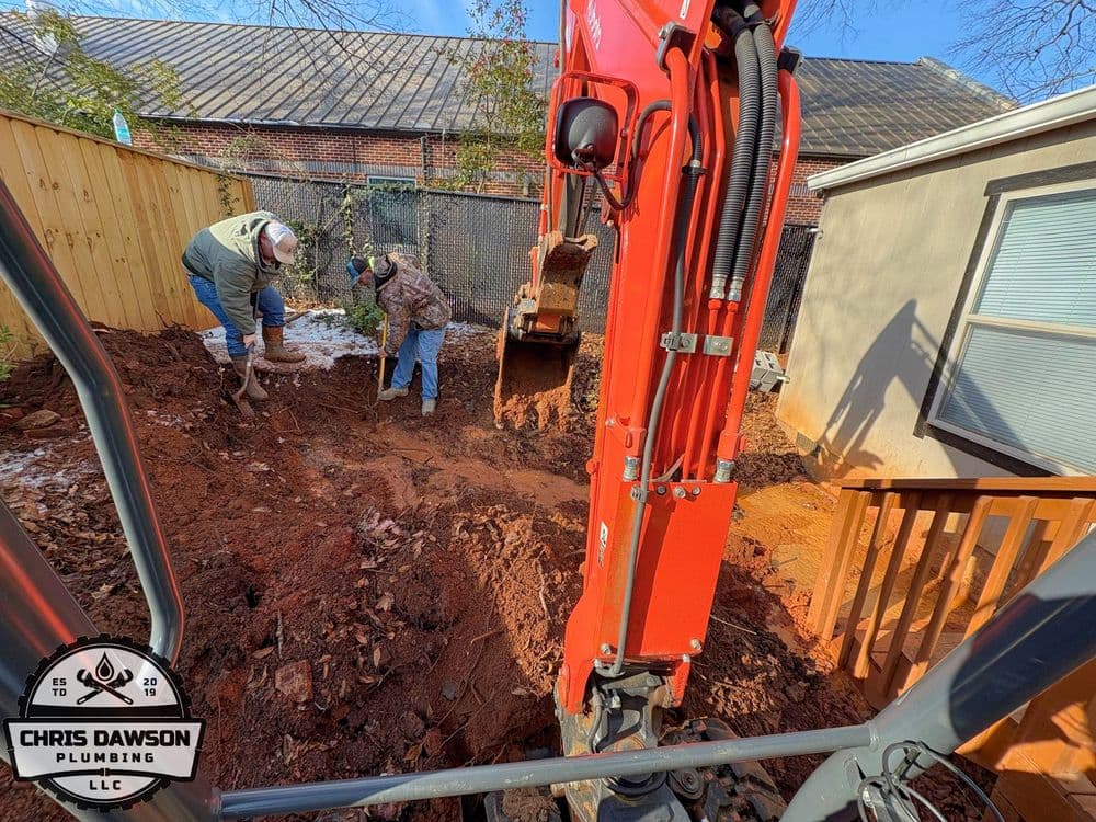 Excavation work in backyard with workers and machinery, plumbing project in progress.
