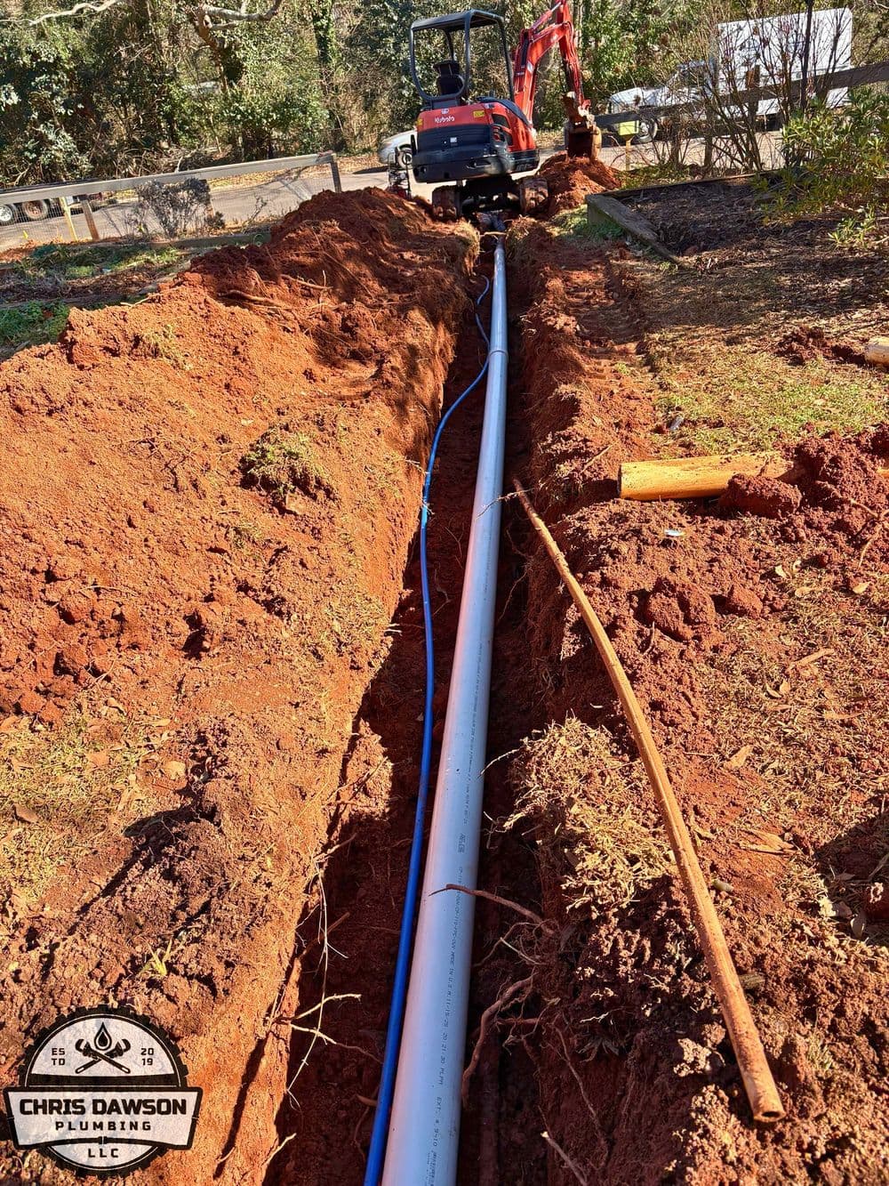 Excavation trench with plumbing pipes being installed in a residential landscape.