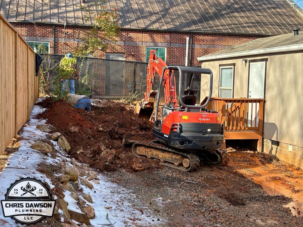 Excavator digging in residential backyard for plumbing work and site preparation.