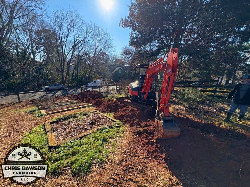 Excavator digging soil for landscaping, with a sunny backdrop and trees in the background.