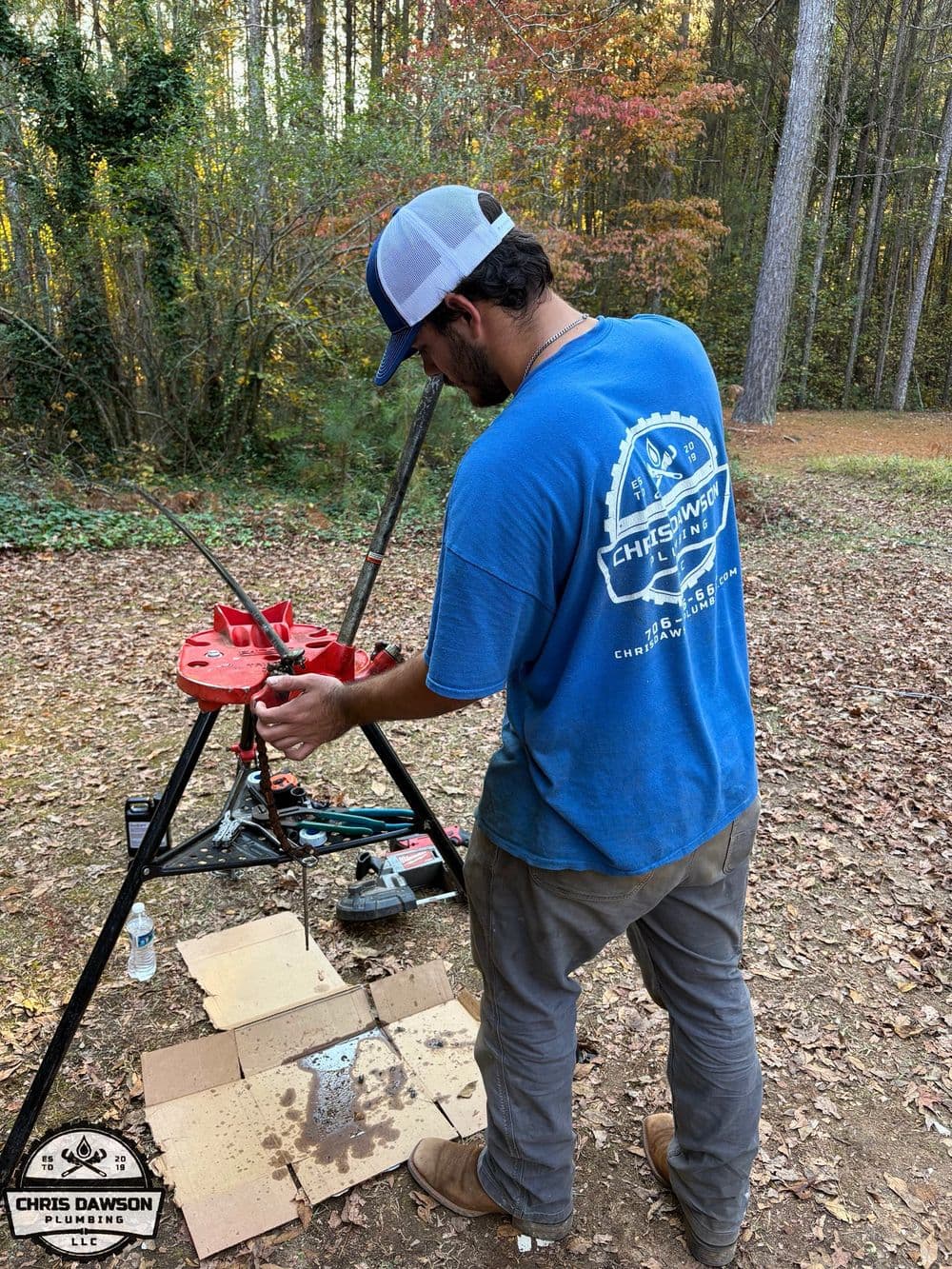 Person in blue shirt working on equipment outdoors with trees in the background.