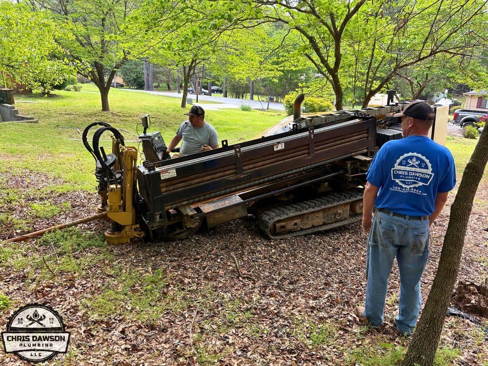 Workers using a trenching machine for plumbing installation in a wooded area.