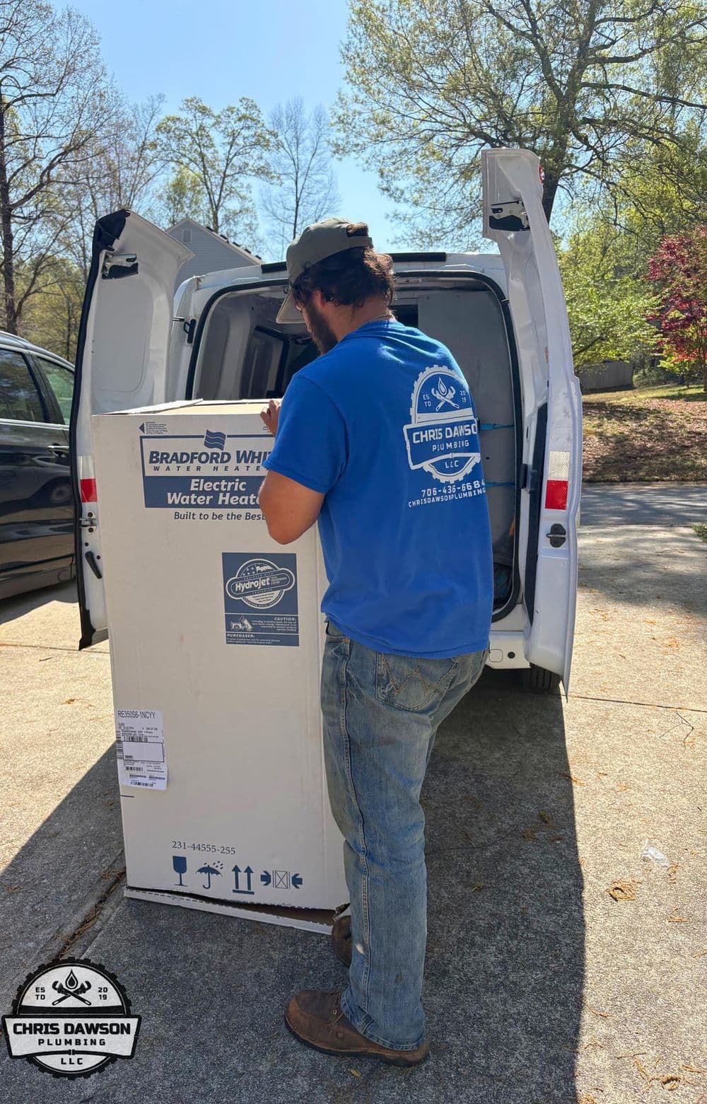 Plumber unloading electric water heater from van in residential area, sunny day.