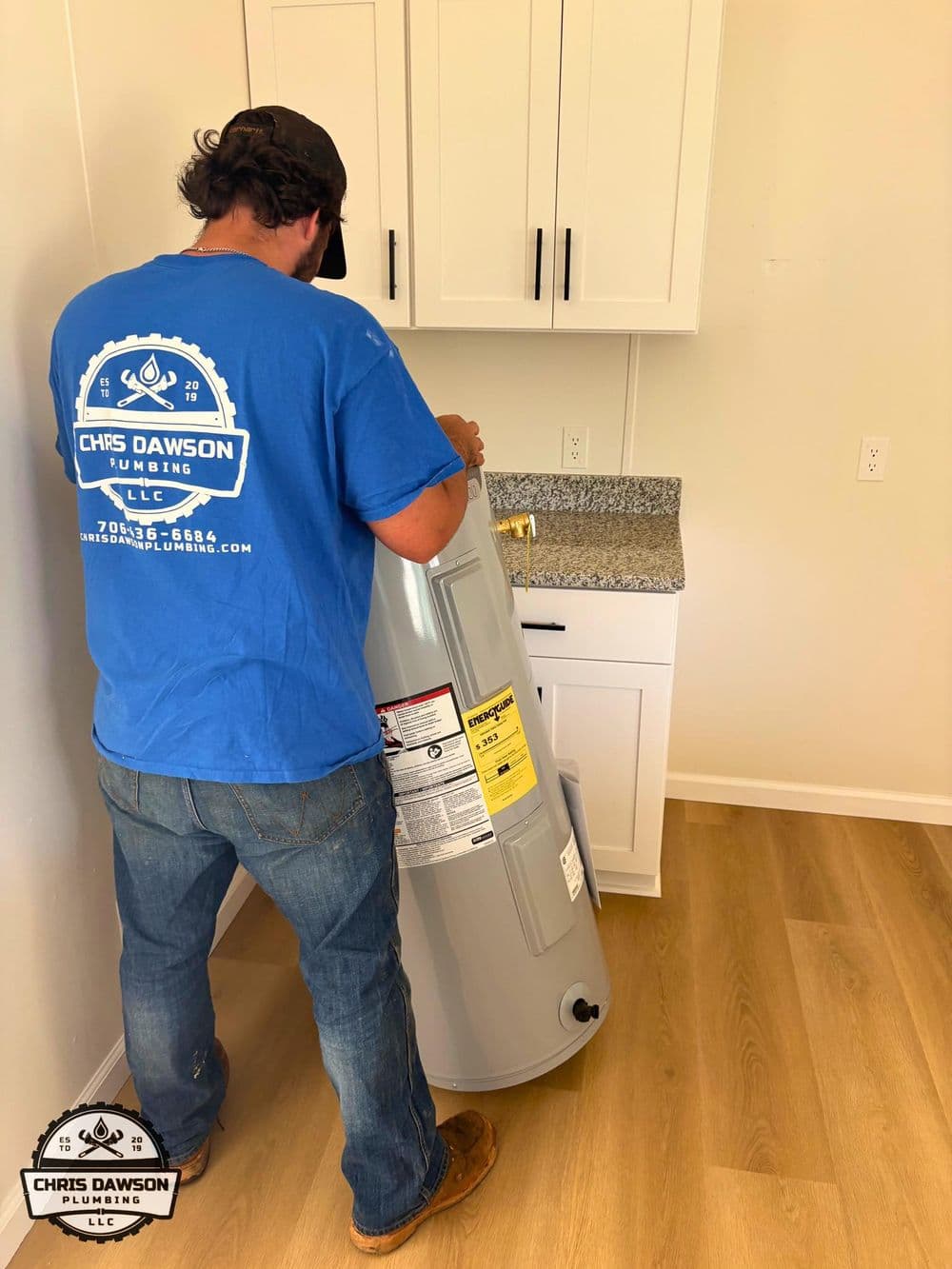 Plumber installs a water heater in a modern kitchen with light wood flooring.